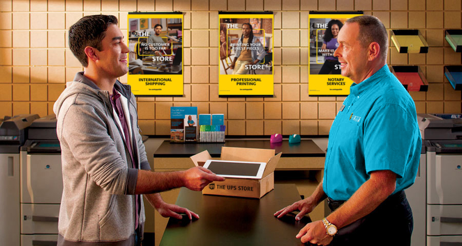 Male customer talking to a male The UPS Store associate, with a tablet packed in a box between them. 